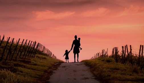 adult and two children walking down a dirt road at sunset