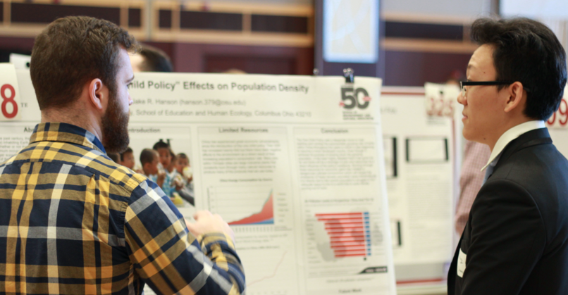 student presenting poster to another student at poster symposium