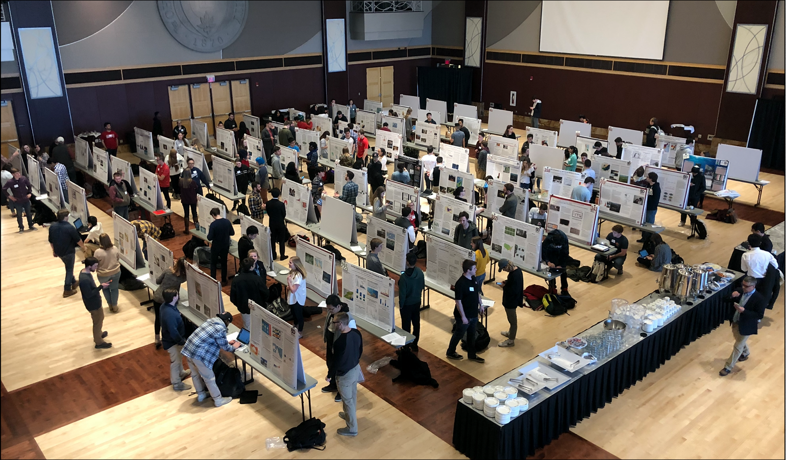 posters set up in rows with students and audience members mingling amongst them