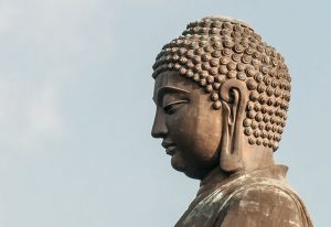 Image of a side profile of Buddha statue in front of a light blue sky.