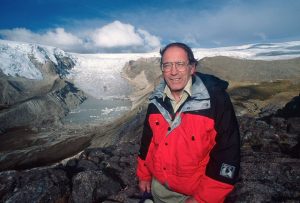 Image of Lonnie Thompson wearing a red coat in front of a glacier.