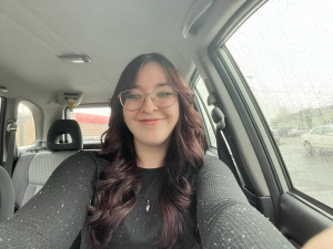 A selfie of a young woman with dark hair sitting in a car.