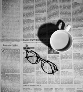 A black and white news paper with glasses and a mug sitting on top.