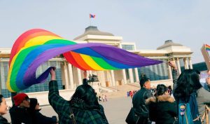 An individual waves a pride flag in front of the Great Khural.