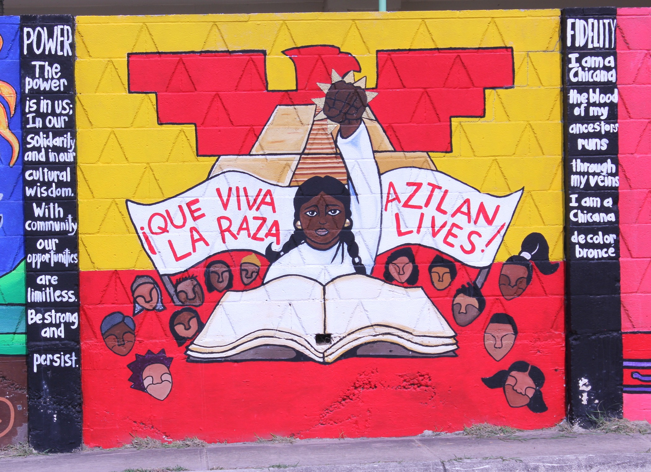 Mural titled "Que viva la Raza," located on the Westside, San Antonio. In the middle, there is a dark-skinned girls with two braids with a fist raised and an open book.