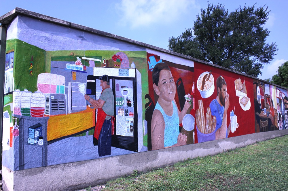 Picture of a long mural. It shows a male vendor selling aguas frescas and a child and man eating churros and ice cream.