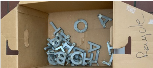 A photograph of metal letters in a brown cardboard box.