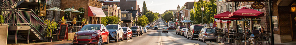 A street with cars parked and cafes.