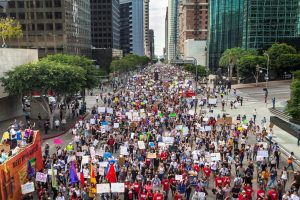 A crowd of protestors marching in an urban, downtown environment.