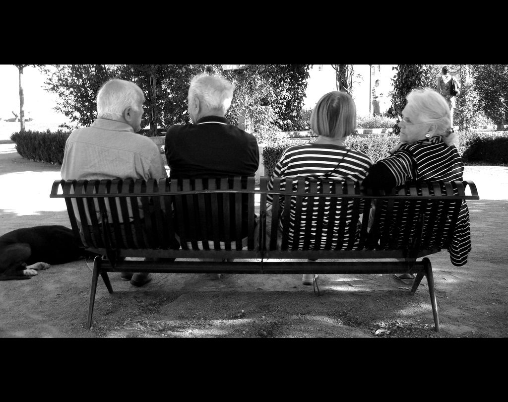 a black and white phote of two elderly couples on a bench