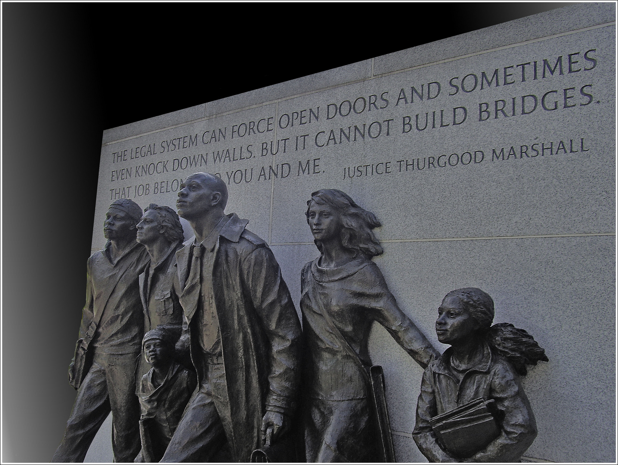 Statues of 4 adults and 2 children in front of a wall with the engraved quotation from Justice Thurgood Marshall that reads, "The legal system can force open doors and sometimes even knock down walls, but it cannot build bridges. That job belongs to you and me."