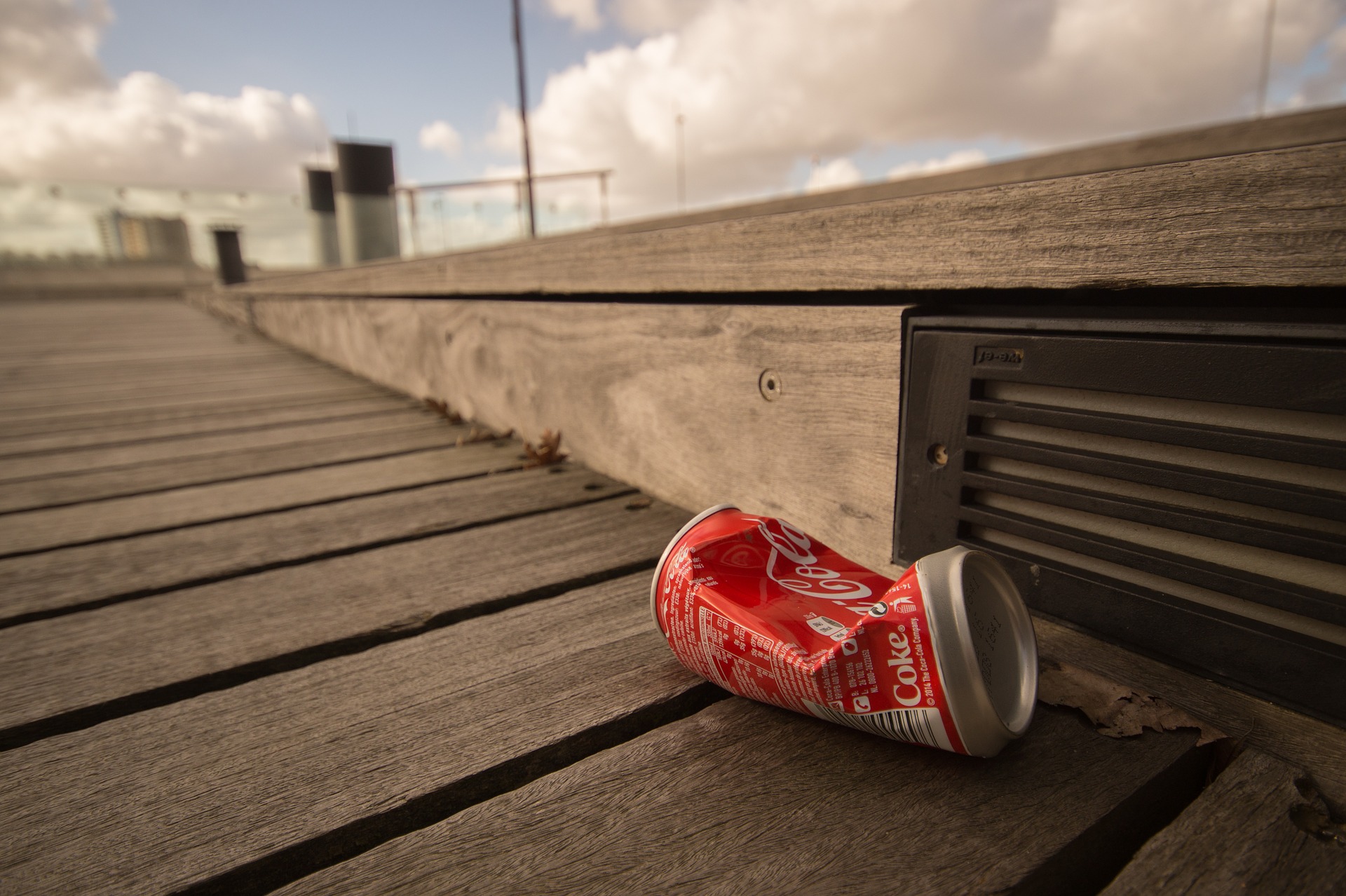 crushed Coke can laying on a wooden dock under a cloudy sky