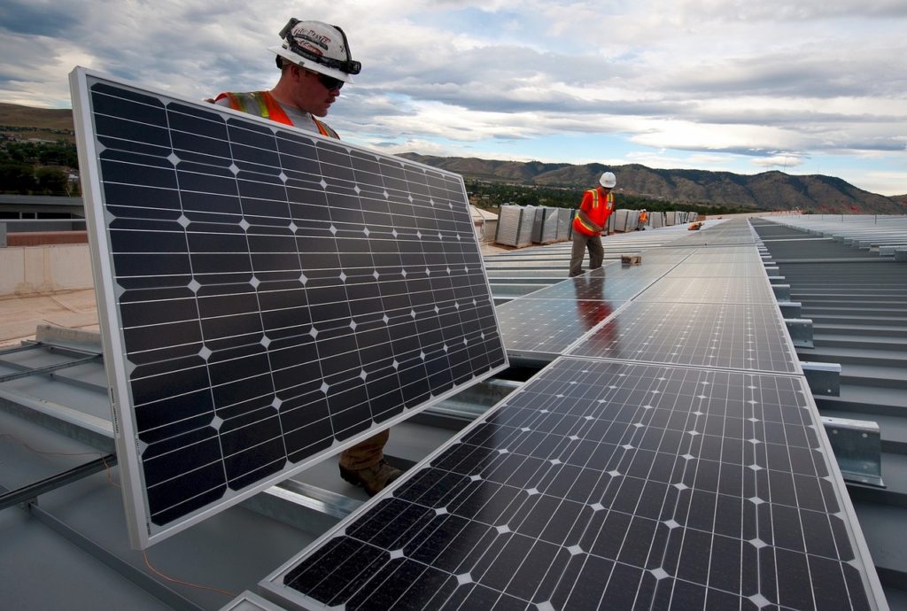 Two workers with reflective vests work on a rooftop to construct a photovoltaic system.